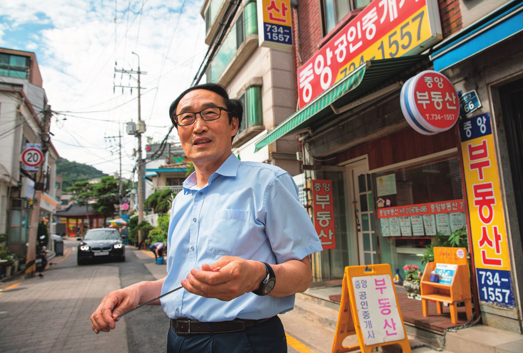 조강희 씨가 15년째 운영하고 있는 자신의 공인중개사 사무소 앞에서 서촌에 대해 설명하고 있다. Ông Cho đứng trước Văn phòng môi giới bất động sản Chungang mà ông đã quản lý 15 năm, giải thích về khu vực trong và ngoài Seochon.