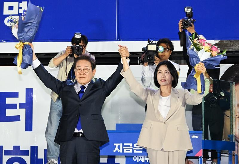 ▲더불어민주당 이재명 대선 후보와 부인 김혜경 여사가 당선이 확실시 된 4일 새벽 서울 여의도 국회 인근에서 당 주최로 열린 국민개표방송 행사에 참석해 꽃다발을 받고서 시민을 향해 두 팔을 들어 인사하고 있다. Tân Tổng thống Hàn Quốc Lee Jae-myung (bên trái) và phu nhân Kim Hye-kyung ở khu Yeouido, thành phố Seoul vào sáng ngày 4/6/2025. (Ảnh: Yonhap News)