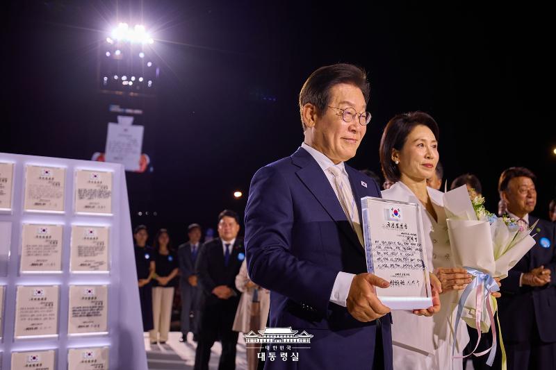 ▲ 이재명 대통령과 김혜경 여사가 15일 서울 세종대로 광화문광장에서 열린 제21대 대통령 국민임명식 '광복 80년, 국민주권으로 미래를 세우다' 행사에서 국민대표 80인으로부터 받은 '국민임명장'을 들어 보이고 있다. Tổng thống Hàn Quốc Lee Jae Myung và Đệ nhất phu nhân Kim Hea Kyung trong lễ nhậm chức Tổng thống Hàn Quốc thứ 21 diễn ra ở quảng trường Gwanghwamun, quận Jongno-gu, thành phố Seoul vào ngày 15/8/2025. (Ảnh: Văn phòng Tổng thống Hàn Quốc - 대한민국 대통령실)